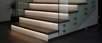 Eine Treppe mit Glasgeländer, LED-Leuchten und Produkten. Lauer maler & raumdesign - Bodenbeläge, Vinylboden, Farben, Sonnenschutz, Malerarbeiten - Bahnhofstr. 5a - 36280 Oberaula